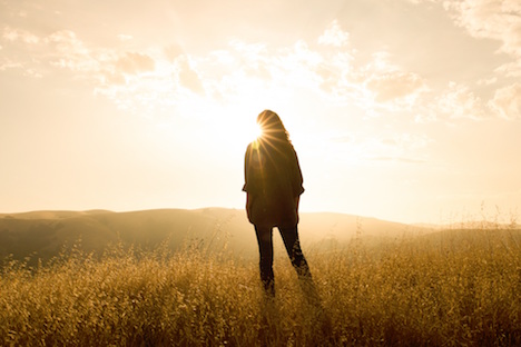 Woman standing in a field and looking toward the sun. 